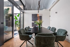 Una sala riunioni moderna con un tavolo rotondo, sedie grigie imbottite e un vaso con fiori.