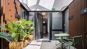 En modern hotellobby med ett glastak, krukväxter, en receptionsdisk och en sittgrupp.