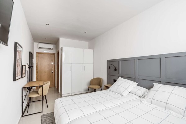 A modern hotel room with a large bed, a desk, and a chair. There is a wardrobe and an air conditioning unit on the wall. - Chamberi Standard Studio (Madrid)