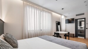 Ένα σύγχρονο δωμάτιο ξενοδοχείου με ένα μεγάλο κρεβάτι, ένα μικρό τραπέζι και μια τηλεόραση.
