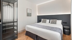 Een moderne slaapkamer met een bed, een nachtkastje, een inbouwkast en een wandlamp.