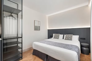 A modern bedroom with a bed, a side table, a built-in shelving unit, and a wall-mounted light fixture. - Pac Fico Deluxe King Suite Near Retiro (Madrid)