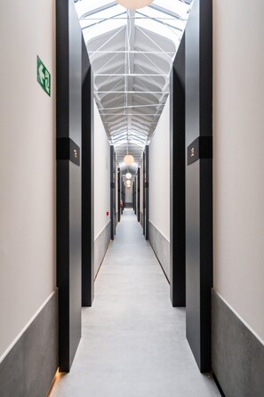 A modern hotel corridor with a skylight ceiling, emergency exit sign, and elevator doors. - Pac Fico Deluxe King Suite Near Retiro (Madrid)