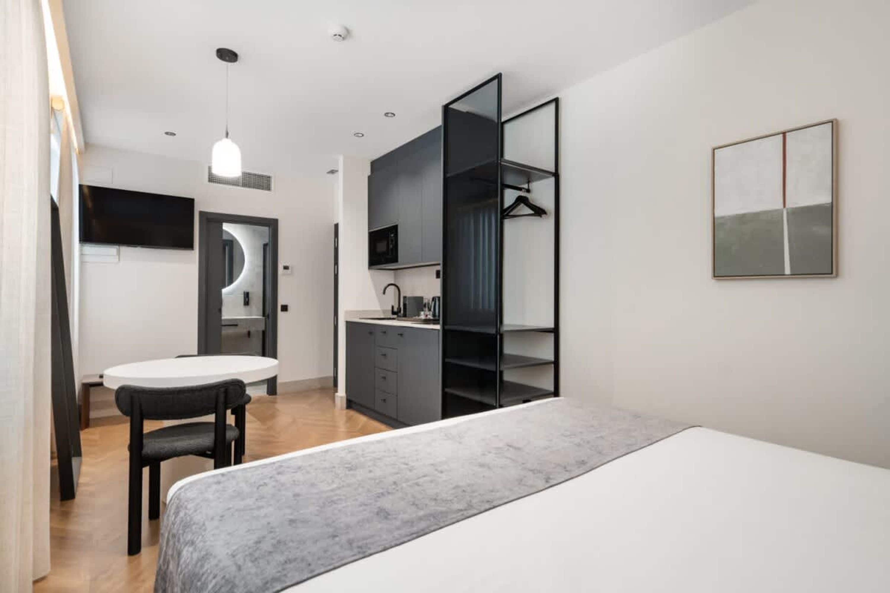 Une chambre d’hôtel moderne équipée d’un lit, d’un bureau avec une chaise, d’une kitchenette et d’une armoire.