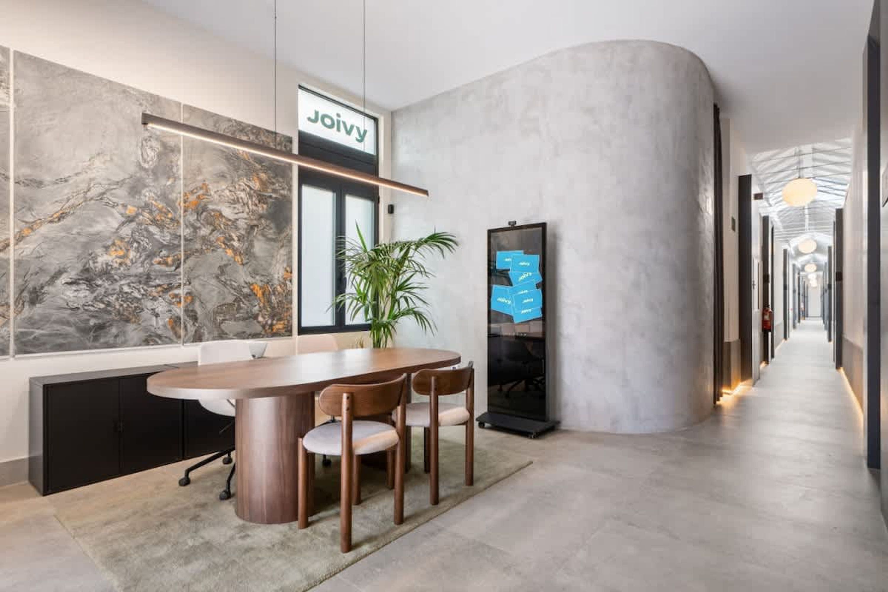 Un espacio de oficina moderno con una amplia pared de mármol, una mesa de conferencias y una pantalla digital.