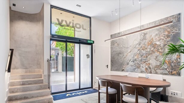 Een moderne hotel lobby met een grote marmeren wand, een houten vergadertafel en een trap.