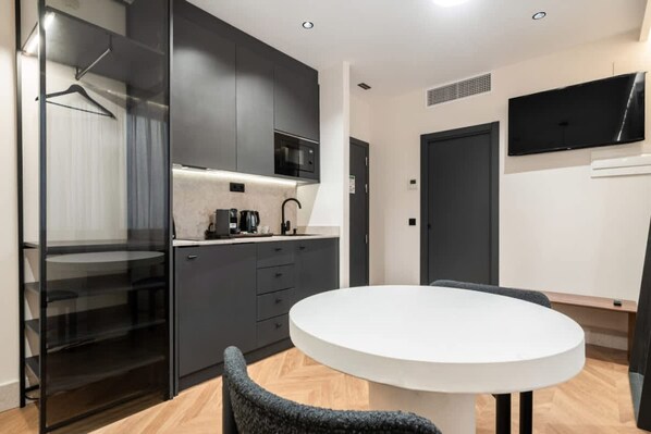 Une cuisine moderne avec des meubles de couleur sombre, un plan de travail blanc et une table de salle à manger ronde, accompagnée d’une chaise.