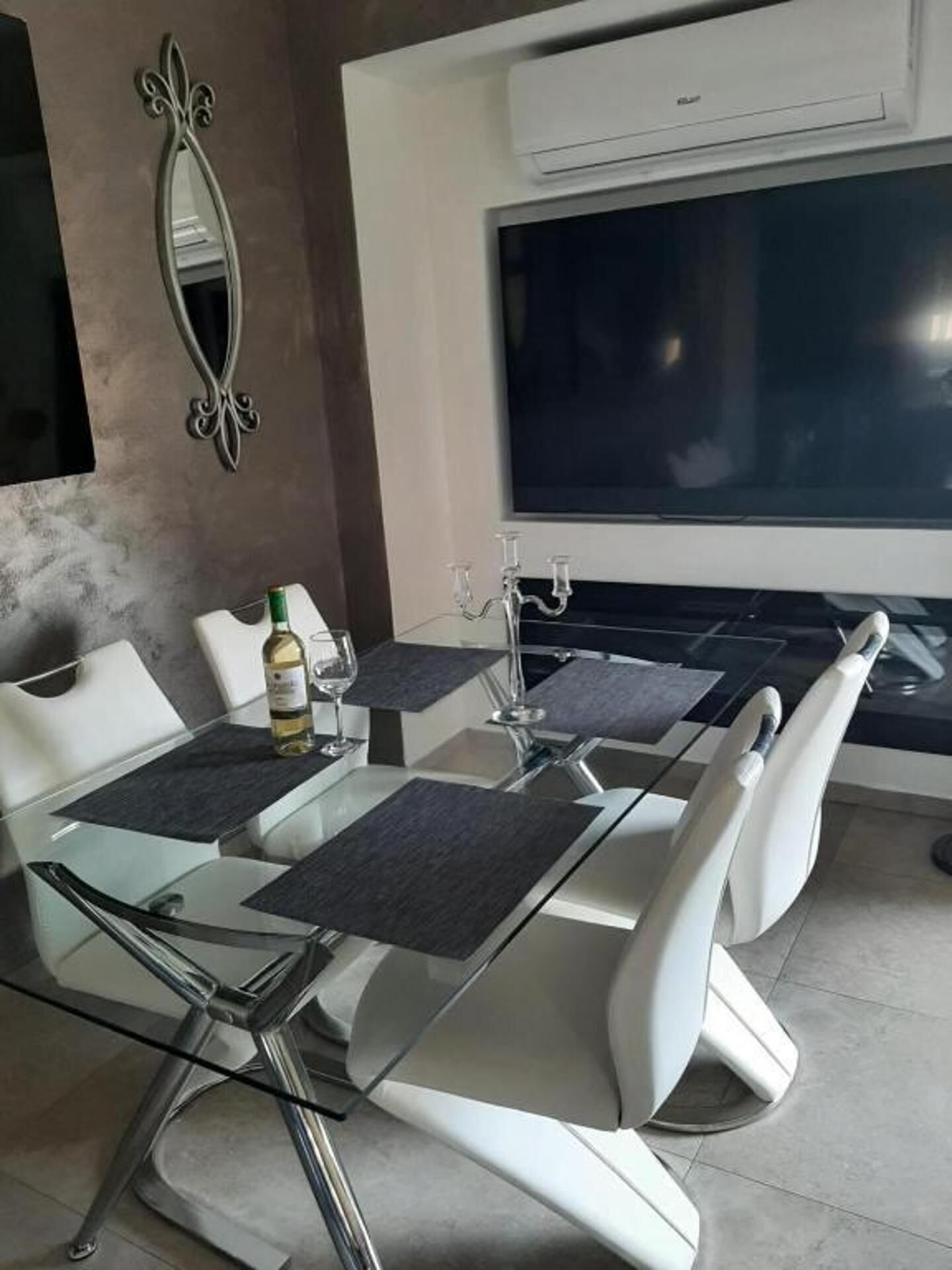A modern dining area with a glass table, white chairs, and a large window.