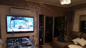 A modern living room with a glass dining table, a large flat-screen TV, a sofa, and a coffee table. - Seaside Bliss Apartment in Daimus (Daimuz)