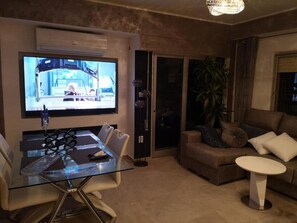 A modern living room with a glass dining table, a large flat-screen TV, a sofa, and a coffee table. - Seaside Bliss Apartment in Daimus (Daimuz)