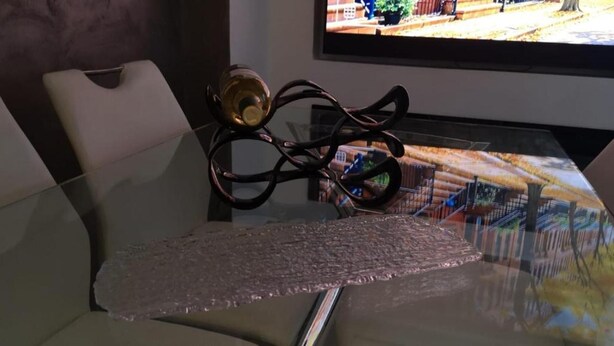 A glass table with a clear plastic cover, a chair with a white cushion, and a decorative metal sculpture. - Seaside Bliss Apartment in Daimus (Daimuz)