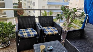 A balcony with two wicker chairs and a small table, a potted plant, and a view of buildings. - Seaside Bliss Apartment in Daimus (Daimuz)