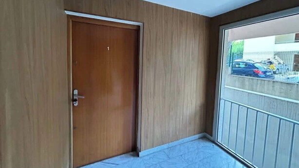 Una habitación con puerta de madera, un balcón con barandilla de metal y vista a coches estacionados afuera.