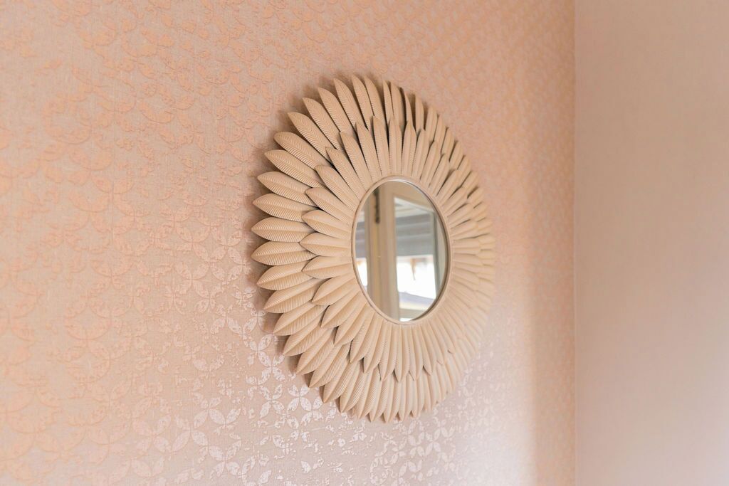 En væg med et detaljeret blomstermønster og et rundt spejl med et solstråle-design.