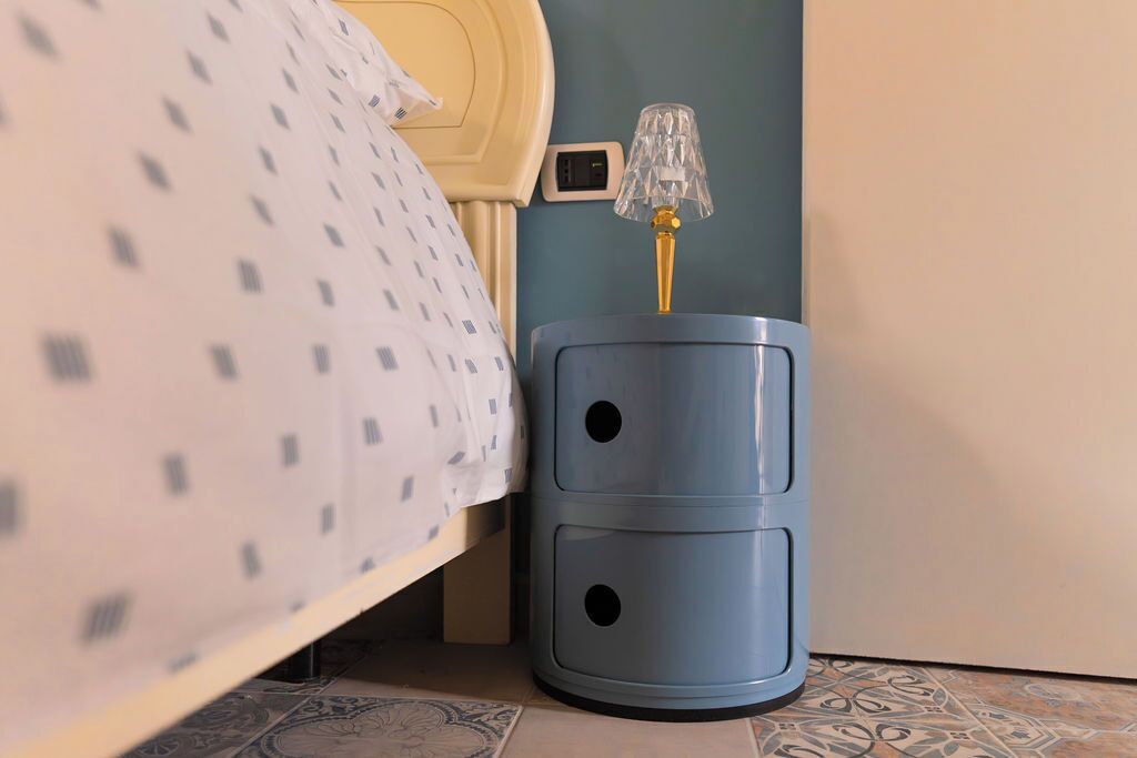Una cama con una colcha estampada, una lámpara de noche y un enchufe de pared.