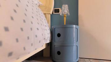 A bed with a patterned bedspread, a bedside lamp, and a wall socket.