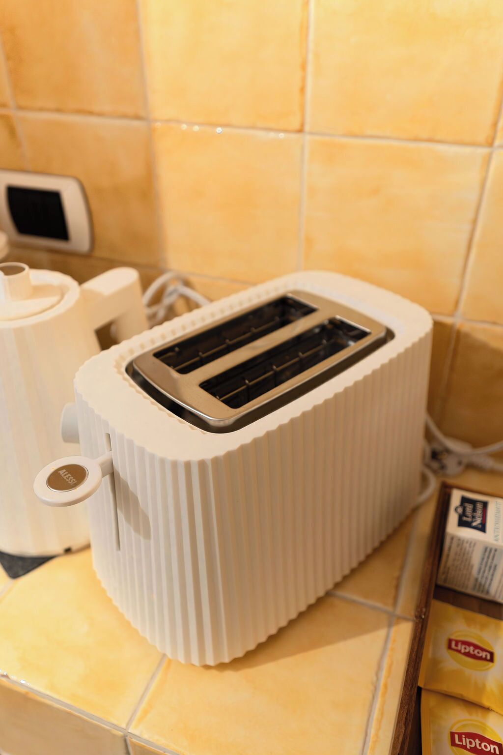 Un tostador blanco sobre una encimera de cocina con un salpicadero de azulejos amarillos.