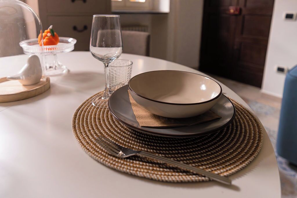 A dining table set with a bowl, plates, a glass, and a fork on a woven placemat.