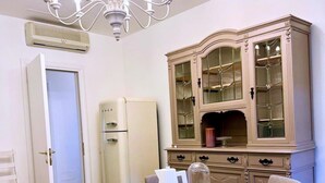 A dining area with a chandelier, a vintage-style cabinet with glass doors, a white table, and a white refrigerator. - Beautiful spacious flat in the old town of Ivrea (Ivrea)