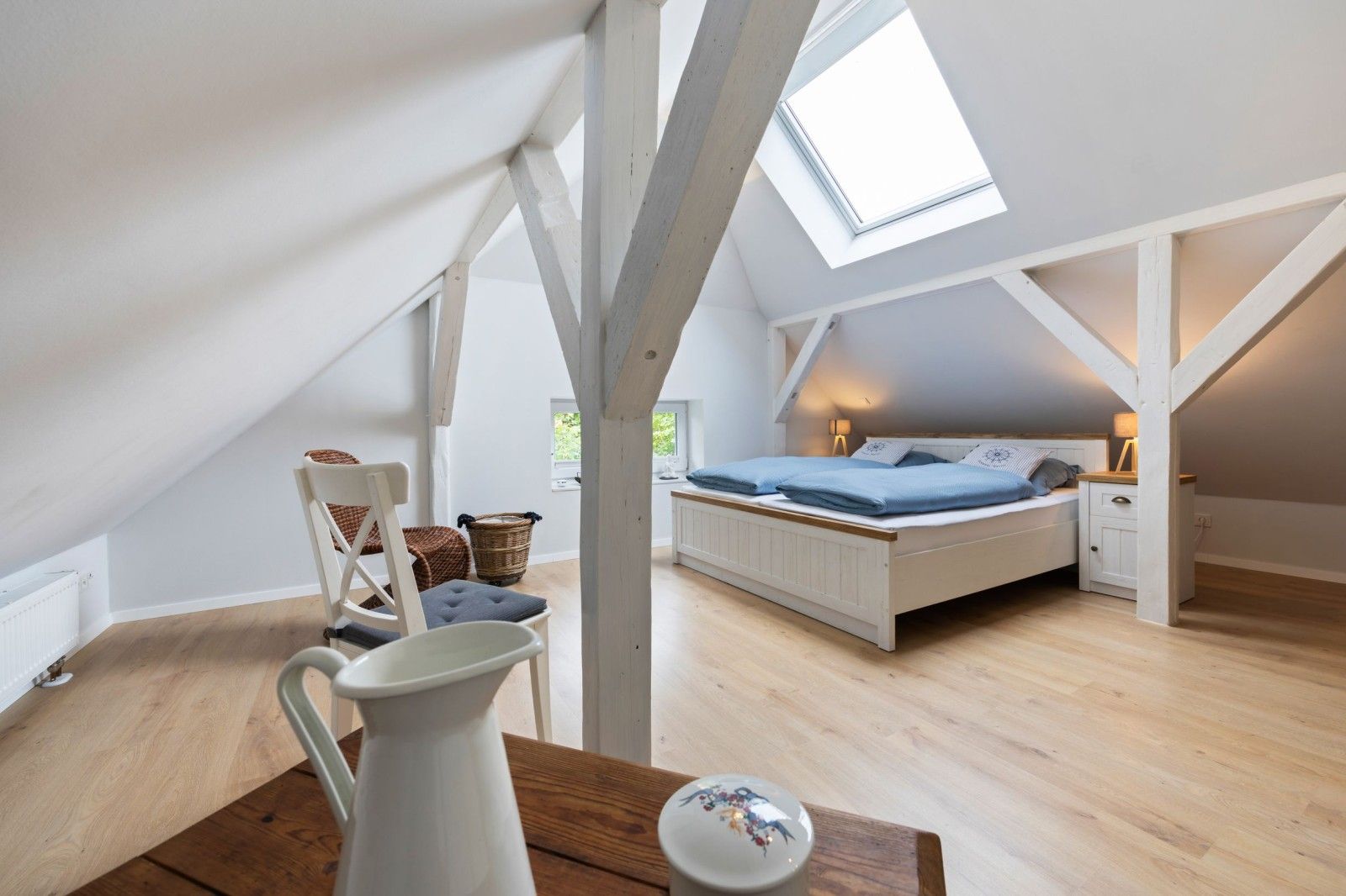A bedroom with a sloped ceiling, a bed, a nightstand, a chair, a table, and a window.