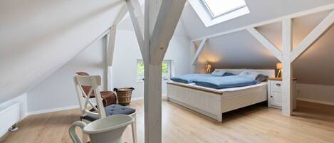 A bedroom with a sloped ceiling, a bed, a nightstand, a chair, a table, and a window.