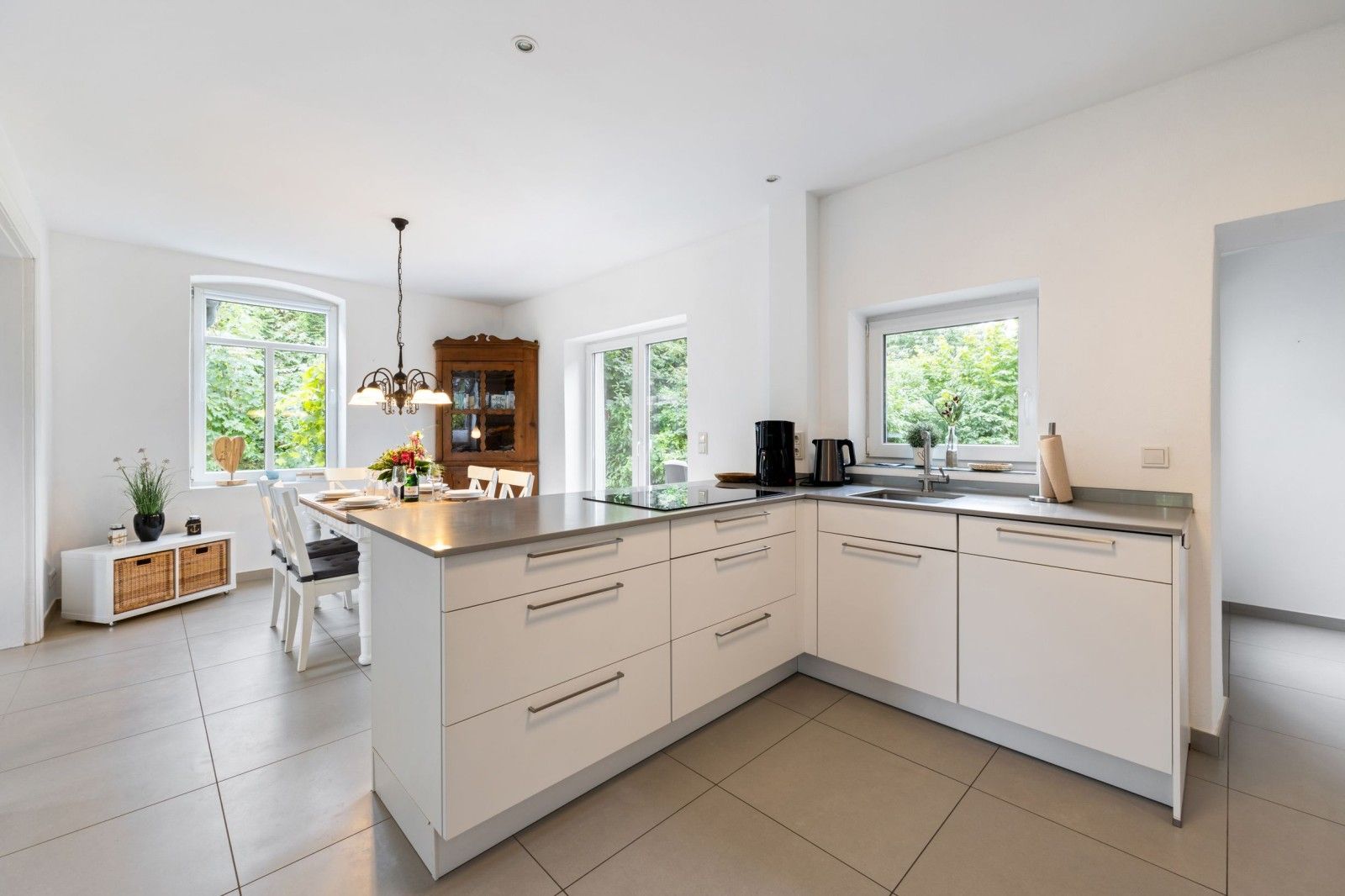A modern kitchen with white cabinetry, a central island, and a dining area with a white table and chairs.