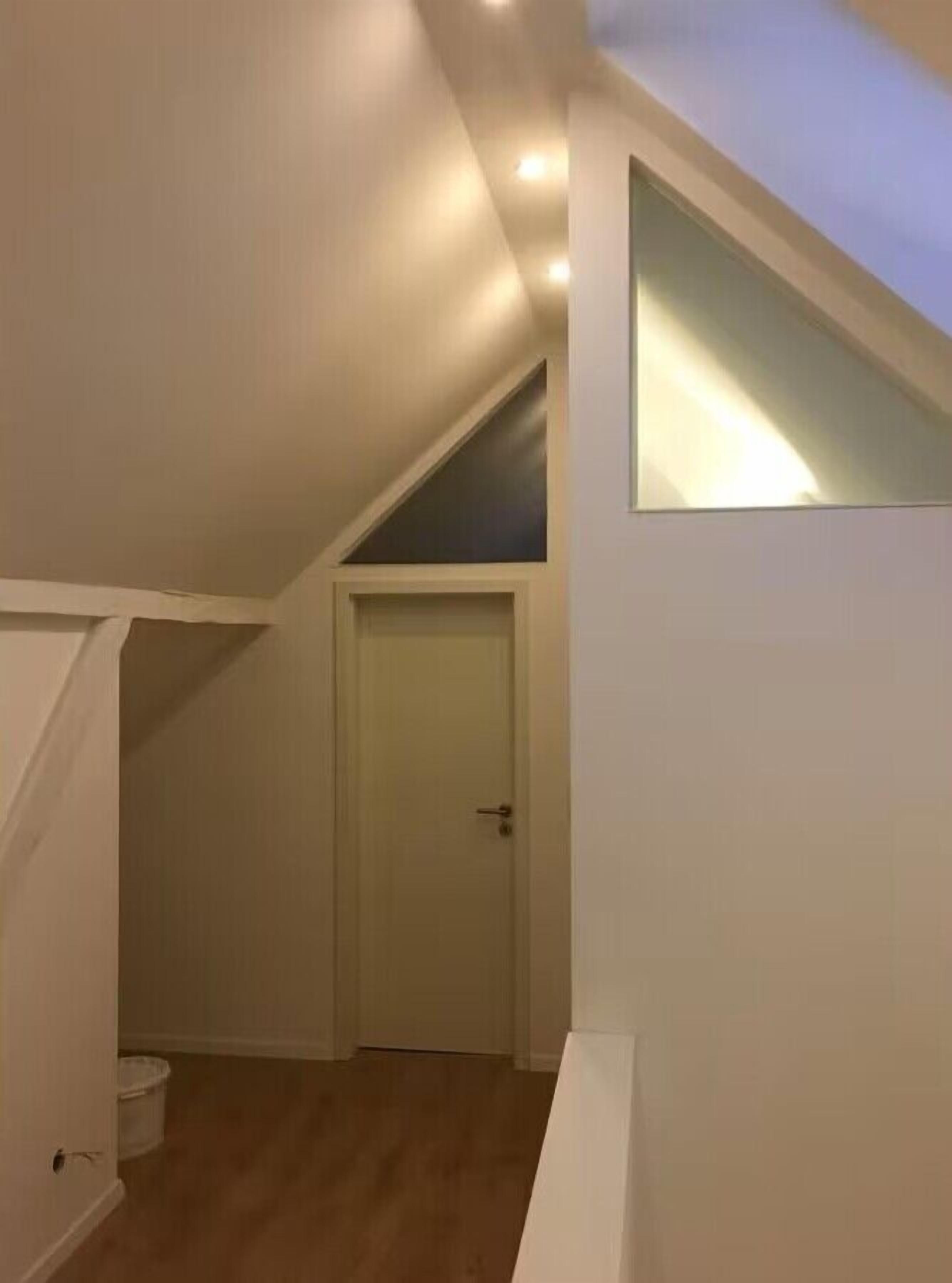 A room with a sloped ceiling, a door, and a small window.