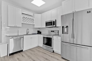 A modern kitchen with white cabinetry, stainless steel appliances, a dishwasher, a microwave, an oven, and a refrigerator. - Modern Stay Minutes from Wynwood & Design District (Miami)