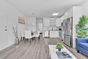 A modern kitchen with white cabinets, stainless steel appliances, and a dining area with white chairs and a glass table. - Modern Stay Minutes from Wynwood & Design District (Miami)