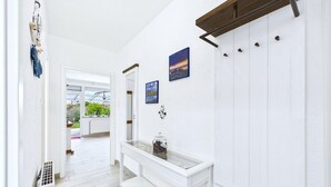 Un couloir avec une console blanche, un porte-manteau et une porte donnant sur une véranda.