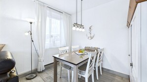 Un coin repas avec une table en bois et des chaises blanches, un lampadaire et une fenêtre agrémentée de rideaux blancs.