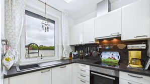Une cuisine moderne avec des meubles blancs, un plan de travail noir, une cuisinière et une fenêtre donnant sur un paysage verdoyant.
