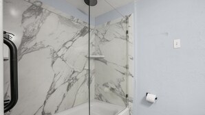 Een badkamer met een douchewand van marmer, een glazen douchecabine en een witte badkuip.