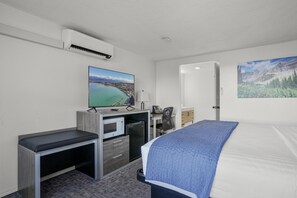 A hotel room with a bed, a desk with a computer, a microwave, and a TV displaying a scenic view. - 1 King Bed, Partial Lake View (Polson)