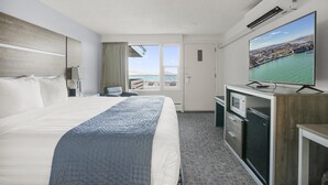 Een hotelkamer met een groot bed, een televisie, een bureau met een magnetron en uitzicht op zee.