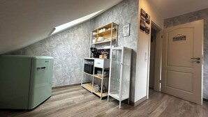 Una cocina compacta con refrigerador integrado, una estantería blanca y una puerta con la etiqueta 'KOMBOS'.