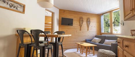 Ein gemütliches Zimmer mit Essecke, einer Couch und einem an der Wand befestigten Fernseher.