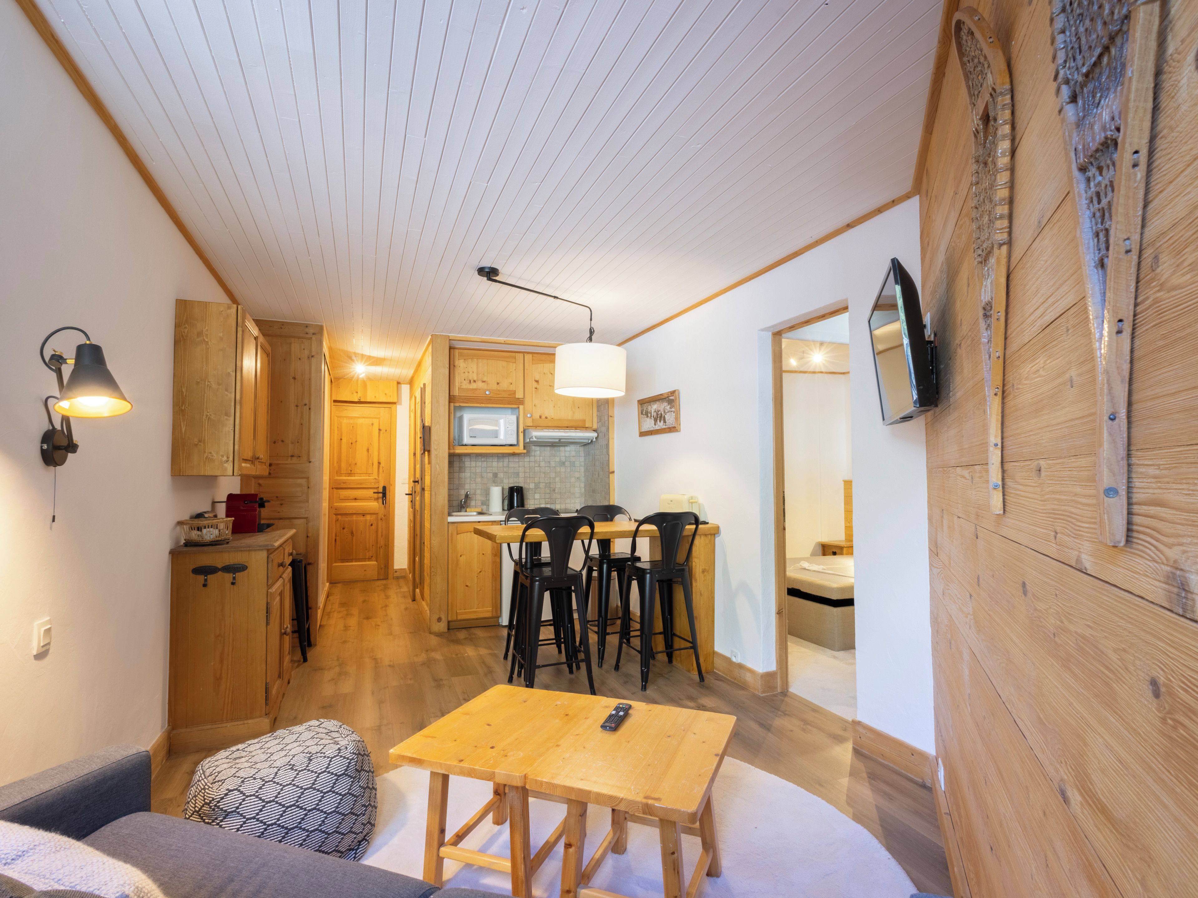 A cozy room with a wooden dining table, a sofa, and a kitchen area with wooden cabinets and a microwave.