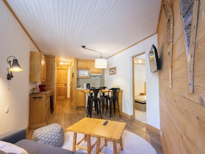 Una habitación acogedora con una mesa de comedor de madera, un sofá y una zona de cocina con armarios de madera y un microondas.