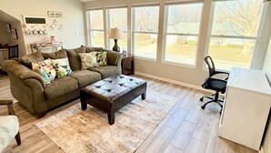 A spacious living room with a large window, a ceiling fan, and a dining area. - Lee's Summit Loft-near downtown (Lee's Summit)
