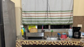 A kitchen with a tiled backsplash, a stainless steel trash bin, a refrigerator, a sink, and various kitchen utensils and appliances.