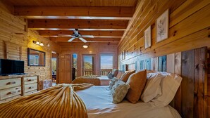 A wooden cabin interior with a bed, a television, and framed pictures on the walls. - 8BR with pvt ensuite deck & baths|Views|Pool|Cinema|A+Location|Pets Ok|Sleep 30+ (Sevierville)