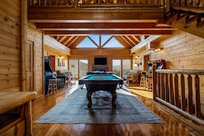 A wooden cabin interior with a pool table, seating area, and a large window. - 8BR with pvt ensuite deck & baths|Views|Pool|Cinema|A+Location|Pets Ok|Sleep 30+ (Sevierville)