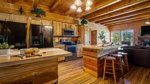 A wooden cabin interior with a kitchen featuring a refrigerator, microwave, stove, and wooden cabinets. - 8BR with pvt ensuite deck & baths|Views|Pool|Cinema|A+Location|Pets Ok|Sleep 30+ (Sevierville)