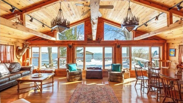 Une cabine spacieuse avec un plafond haut, de grandes fenêtres offrant une vue sur l’océan, un coin salon confortable avec une cheminée et des meubles en bois rustique.