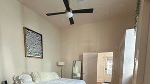 A bedroom with a bed, a ceiling fan, a bedside table, a lamp, a mirror, and a door leading to another room. - The Royal Hideaway- Designer 2BR/2BA, Private Yard (New Orleans)