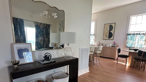 A spacious living area with a wooden floor, a console table with a mirror, a lamp, and storage baskets. A dining area with a table and chairs is visible in the background. - The Royal Hideaway- Designer 2BR/2BA, Private Yard (New Orleans)