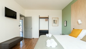 Habitación de hotel con cama, reposabajares, televisor, armario y puerta que da a un balcón.
