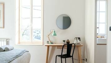 Une chambre à coucher avec un lit, un bureau avec une chaise, un miroir rond et une fenêtre.