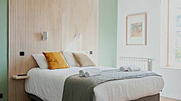 Une chambre à coucher moderne avec une tête de lit en lattes de bois, un lit recouvert d’une couette grise et blanche, et un plancher en bois.